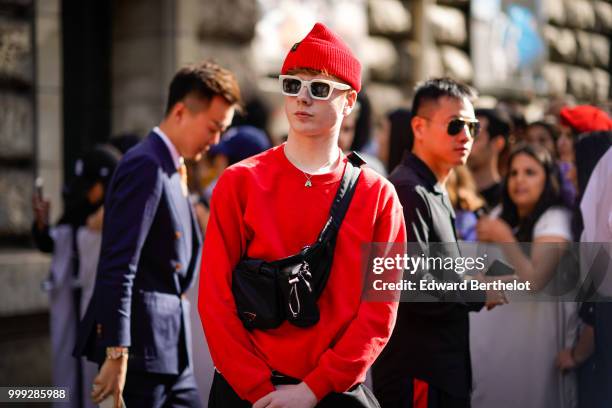 Guest wears a red beanie hat, a red pullover, a black shoulder strap bag, outside Dior, during Paris Fashion Week - Menswear Spring-Summer 2019, on...