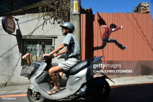 Man rides past street art in "Love Lane", part of Chongjian Street, the oldest street in the Tamsui district of New Taipei City on July 15, 2018. /...