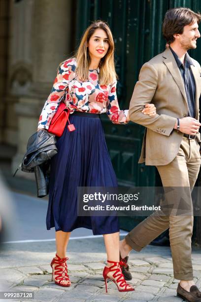Guest wears a flower print shirt, a red bag, a blue pleated skirt, red heels shoes, outside Dior, during Paris Fashion Week - Menswear Spring-Summer...