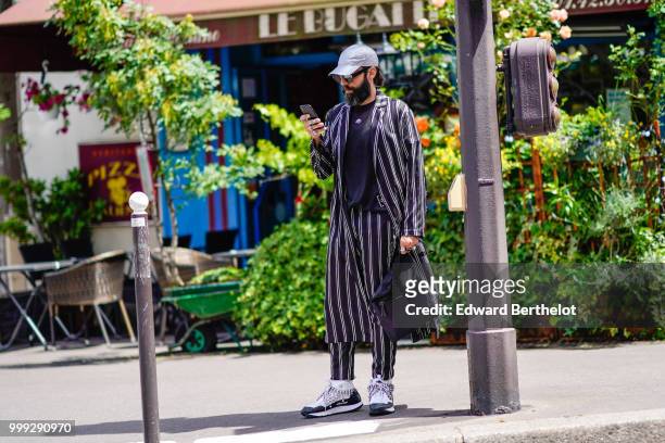 Guest wears a cap, a striped jacket, striped pants, sneakers shoes, outside Wooyoungmi, during Paris Fashion Week - Menswear Spring-Summer 2019, on...