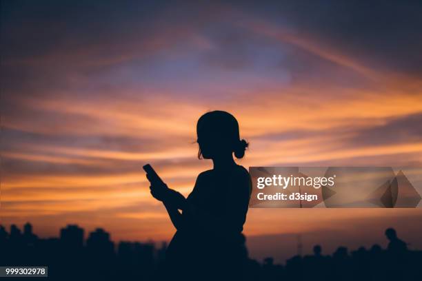 silhouette of pregnant woman using mobile phone against dramatic sky during sunset - street style 2017 stock pictures, royalty-free photos & images