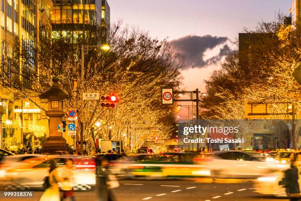 people walk and cars run on aoyama dori street, which street crosses the illuminated omotesando street at sunset at minamiaoyama, minato tokyo japan on december 05 2017. tree lined omotesando street is decorated and illuminated for winter holydays seasons - tree people stock-fotos und bilder