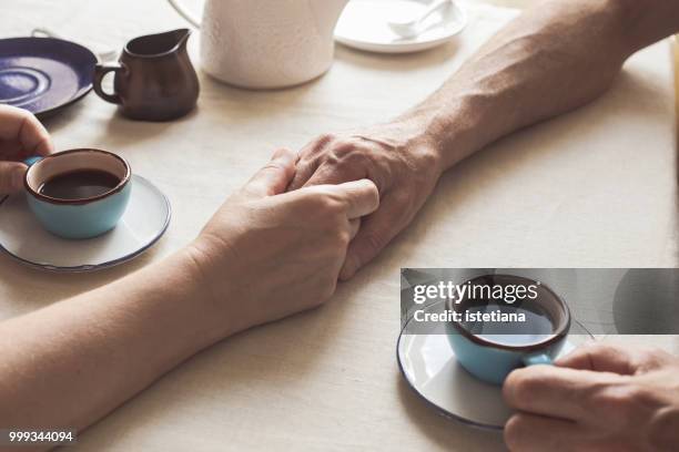 cropped image of senior couple holding hands and drinking coffee - uomo donna per mano foto e immagini stock