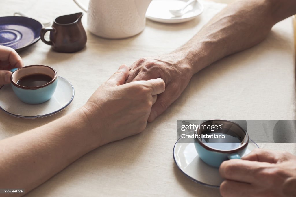 Cropped image of senior couple holding hands and drinking coffee