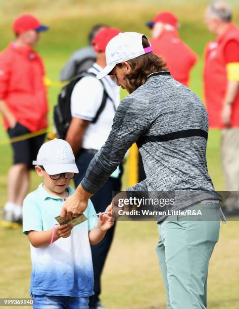 Tommy Fleetwood of England signs autographs for a young fan as he practices during previews to the 147th Open Championship at Carnoustie Golf Club on...