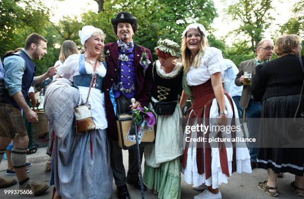 July 2018, Germany, Munich: Women dressed as maids sitting bbeside a man dressed as Ludwig II during the Kocherlball at the Chinesischer Turm . Every...