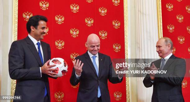 Emir of Qatar Sheikh Tamim bin Hamad Al-Thani holds a ball as Russian President Vladimir Putin and FIFA President Gianni Infantino react during a...