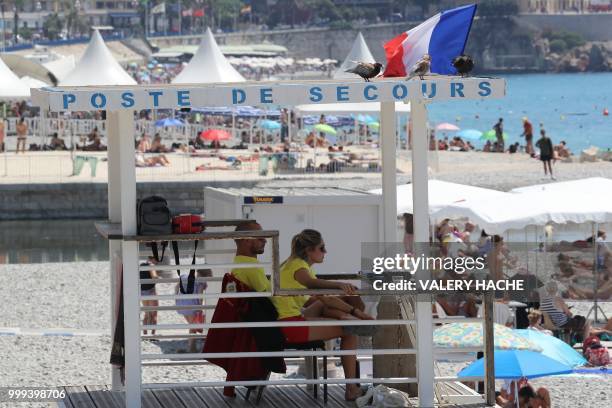 Lifeguards sit in their lifeguard's station as a French flag flutters in the wind in Nice, a few hours prior to the Russia 2018 World Cup final...