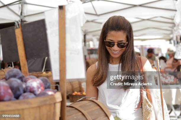 a young ethnic woman shops at the farmers market, on a warm sunny day, wearing sunglasses - mireya acierto stockfoto's en -beelden