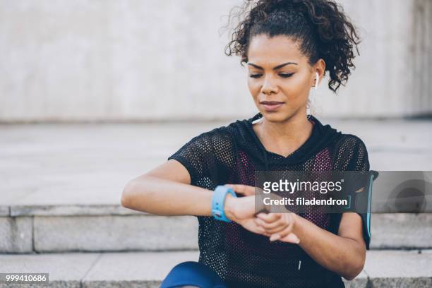 年輕的非洲裔美國婦女檢查她的智慧手錶 - smart 個照片及圖片檔
