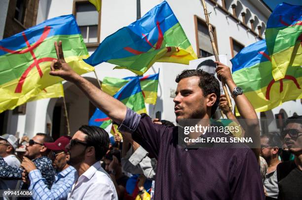 Moroccan protester raises the victory gesture as others behind him wave the Berber, or Amazigh, flag during a protest against the jailing of Al-Hirak...