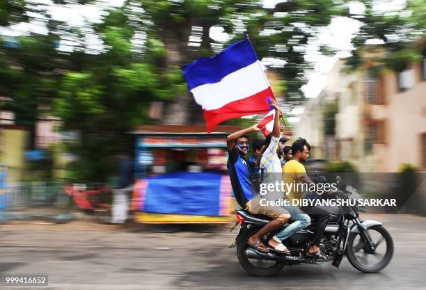 Indian fans of the French football team ride a motorbike as they wave a French national flag ahead of the FIFA 2018 World Cup final match in the...