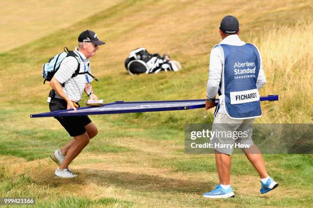 The caddie of Darren Fichardt of South Africa and a volunteer move an advertising sign on hole one during day four of the Aberdeen Standard...