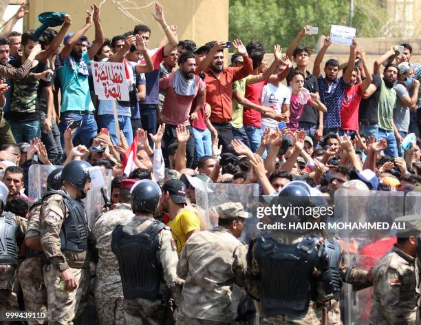 Iraqi riot police lined up as protesters chant slogans and hold up signs during a demonstration in Basra on July 15, 2018. The arabic sign in red at...