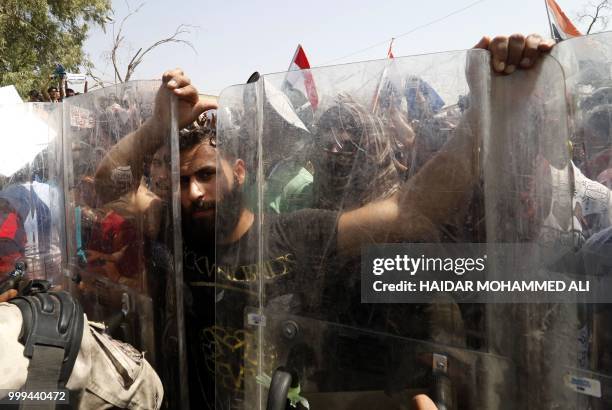 Protester grabs the shields of Iraqi security forces forming a human barrier, during a demonstration against unemployment and a lack of basic...