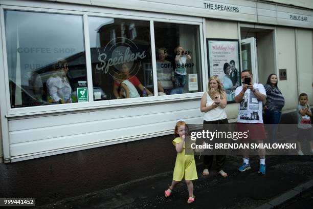 Bystanders watch the motorcade carrying US President Donald Trump as it drives to Glasgow Prestwick Airport, in Maybole, Scotland on July 15 at the...