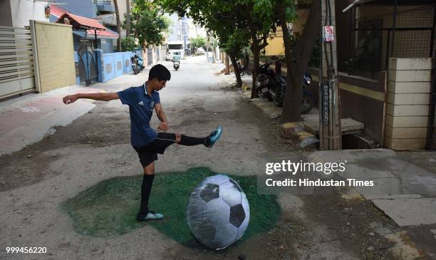 Boy poses with the 3D football painted on a pothole by Baadal Nanjundaswamy at Sultanpalaya, on July 15, 2018 in Bengaluru, India.