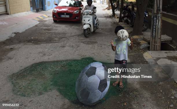 Boy poses with the 3D football painted on a pothole by Baadal Nanjundaswamy at Sultanpalaya, on July 15, 2018 in Bengaluru, India.