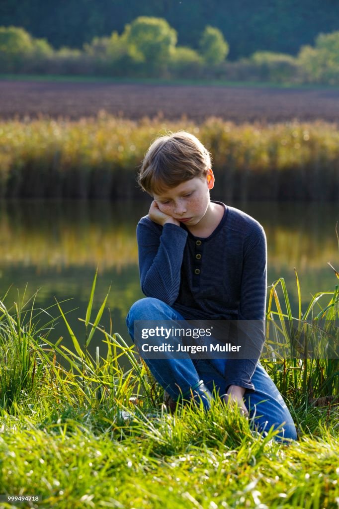 Sad boy sitting on a small lake, Wandersleben, Thuringia, Germany