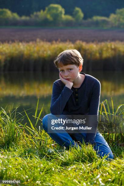 sad boy sitting on a small lake, wandersleben, thuringia, germany - ginger banks stockfoto's en -beelden