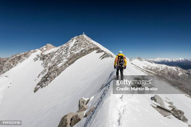 mountaineer on the summit ridge during the ascent of mt hoher weisszint, summit cross at the back, main chain of the alps, zillertal alps, lappach muehlwaldertal valley, tauferer ahrntal valley, puster valley, province of south tyrol, tyrol, trentino-alto - no alto stock-fotos und bilder