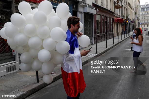 France supporter holds balloons and wears a giant French flag as he celebrates after France won the Russia 2018 World Cup final football match...
