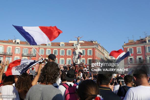 People stand on a statue and wave French flags as they celebrate after France won the Russia 2018 World Cup final football match against Croatia, on...