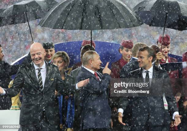 Gianni Infantino, president of FIFA, from left, Vladimir Putin, Russia's president, and Emmanuel Macron, France's president, react as rain falls...