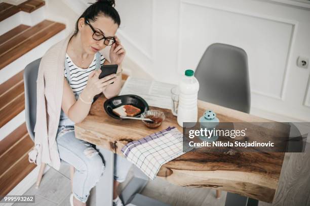 hermosa chica utilizando su teléfono móvil mientras ella está teniendo un desayuno - nikla fotografías e imágenes de stock