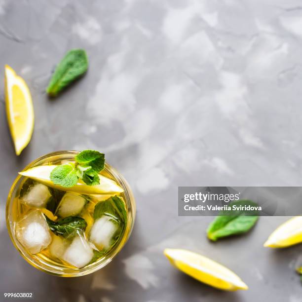 a glass glass with a cold tea with ice, mint and lemon on a gray concrete background. summer... - lemon mint stock pictures, royalty-free photos & images