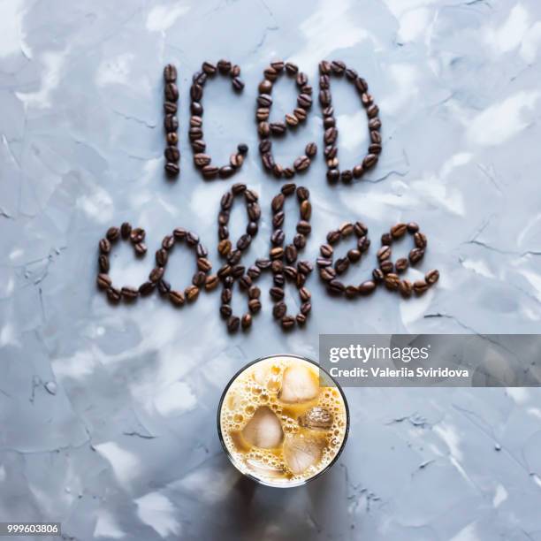 a glass of iced coffee with milk next to the inscription "ice coffee" from coffee beans on a gray... - chalcedony stock pictures, royalty-free photos & images