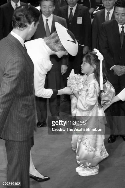 Princess Diana, Princess of Wales receives a flower bouquet from a Japanese girl wearing kimono while Prince Charles, Prince of Wales watches during...