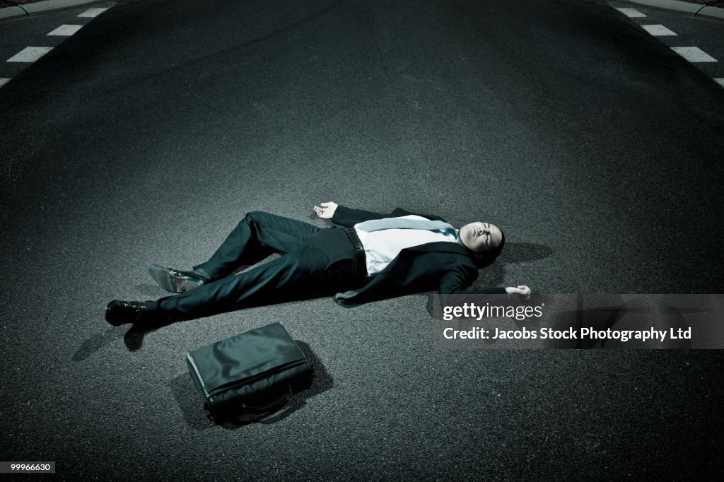 Asian businessman laying on asphalt roadway