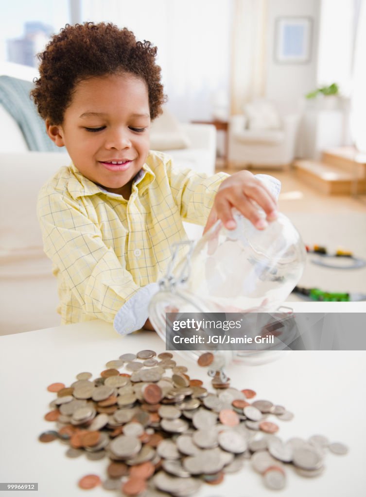 Black boy emptying jar of coins on table