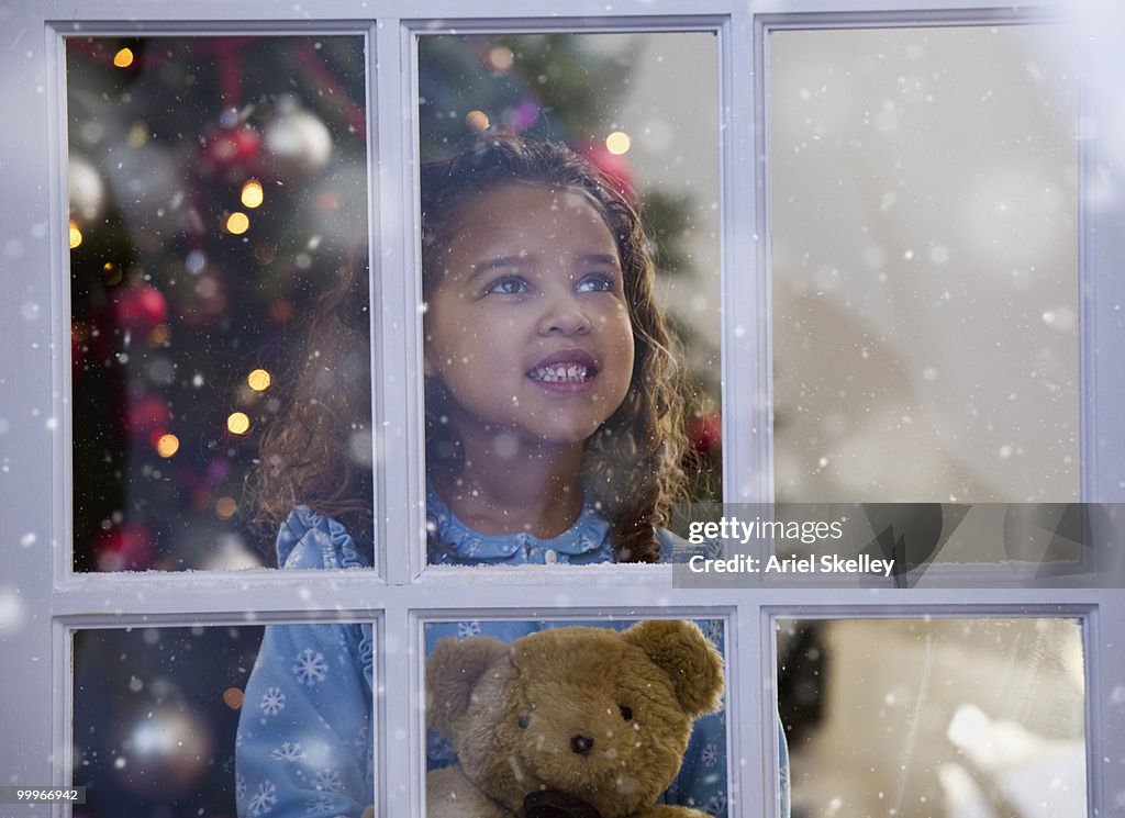 Mixed race girl looking out window at Christmas