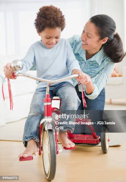 mixed race woman teaching son to ride tricycle - driving barefoot stock pictures, royalty-free photos & images