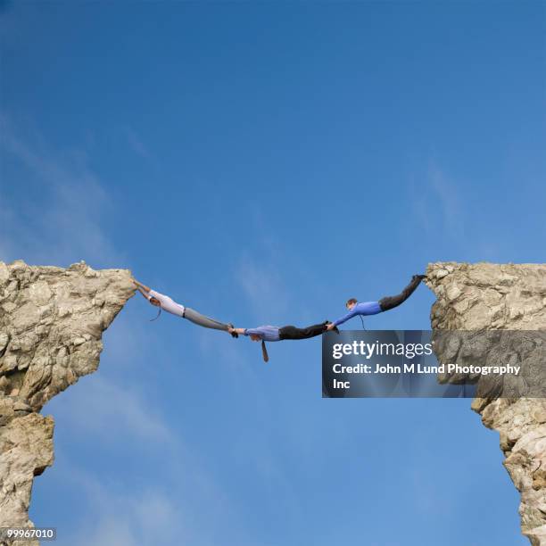 businessmen holding hands and feet to bridge cliffs - bridging the gap concepts -heart stock pictures, royalty-free photos & images