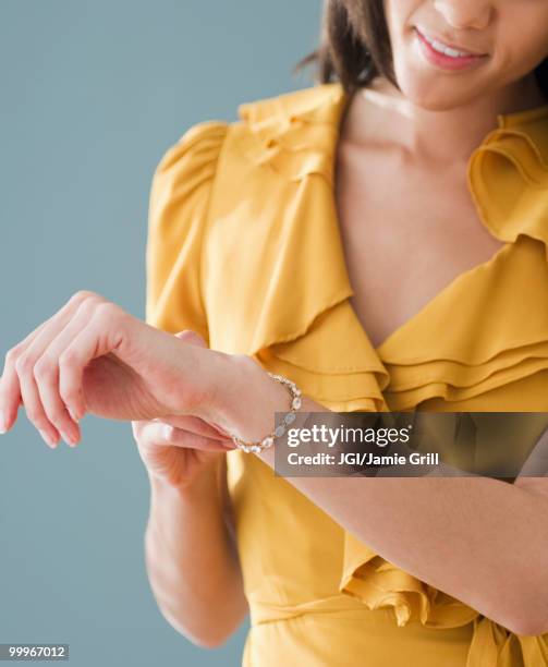 mixed race woman putting on bracelet - bracelet stock pictures, royalty-free photos & images