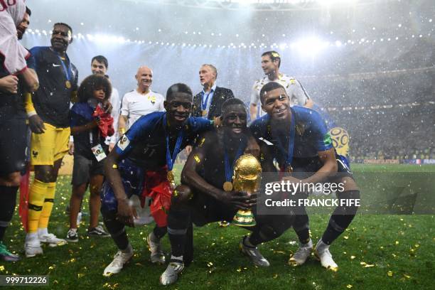 France's defender Benjamin Mendy holds the World Cup trophy between France's forward Ousmane Dembele and France's forward Kylian Mbappe after winning...