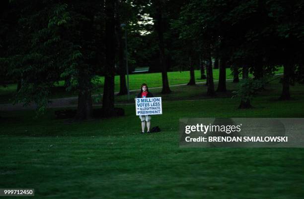 Protester holds a sign reading "3 millions votes less = illegitimate President" while watching as a motorcade with US President Donald Trump and US...