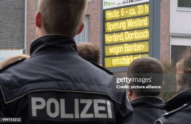 Police officers wait near the finding place of the aerial bomb, looking at a traffic infromation sign in wait of the defusion in Frankfurt am Main,...