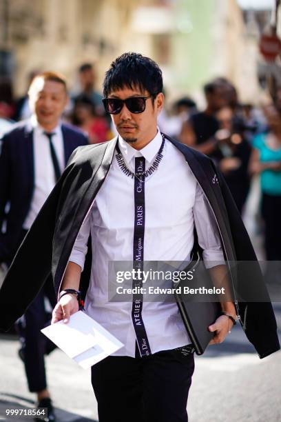 Guest wears a black jacket, sunglasses, a Christian Dior "atelier" white shirt, a black clutch, outside Dior, during Paris Fashion Week - Menswear...