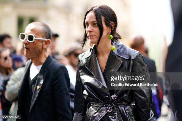 Guest wears green earrings and a black pvc trench coat, outside Dior, during Paris Fashion Week - Menswear Spring-Summer 2019, on June 23, 2018 in...
