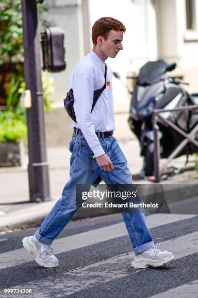 Guest wears a white pullover, a shoulder strap bag, blue jeans, white sneakers shoes, outside Wooyoungmi, during Paris Fashion Week - Menswear...