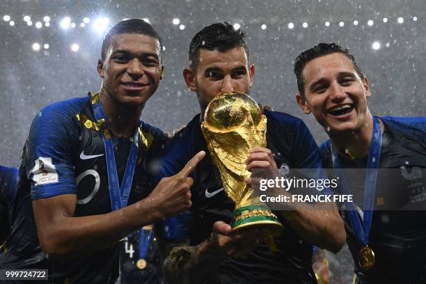 France's defender Lucas Hernandez kisses the World Cup trophy between France's forward Kylian Mbappe and France's forward Florian Thauvin after...