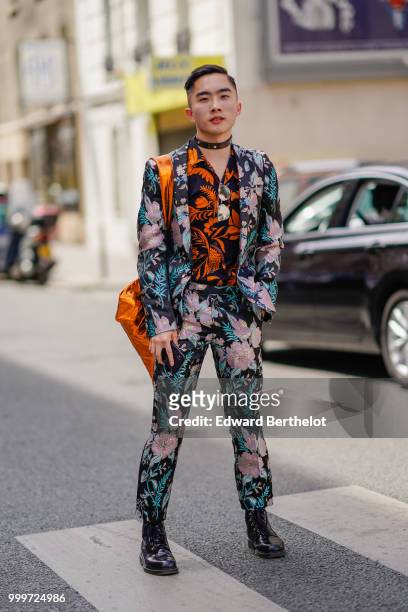 Guest wears a flower print blazer jacket, floral print pants, black leather shoes, and orange and black shirt, a choker, outside Wooyoungmi, during...