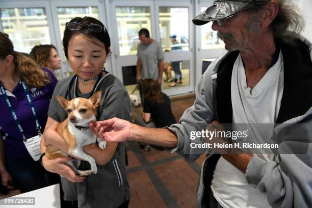 Veterinarian Dr. Yuko Martin, left, checks out Tinkerbell a 9 year old Chihuahua owned William Nicol, right, during an on-site street clinic outside...