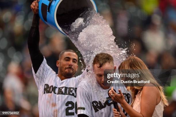 Trevor Story of the Colorado Rockies is doused with ice water by Ian Desmond as he gives a TV interview to Taylor McGregor, after hitting a...
