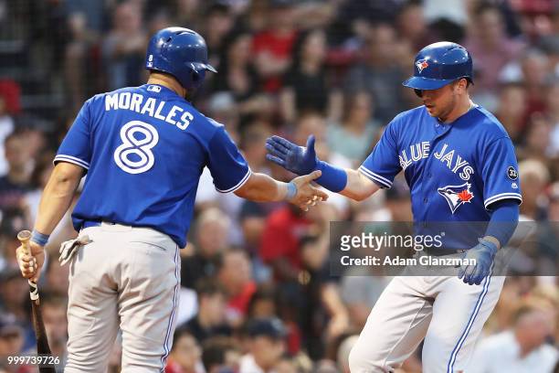 Justin Smoak high fives Kendrys Morales of the Toronto Blue Jays after scoring in the third inning of a game against the Boston Red Sox at Fenway...