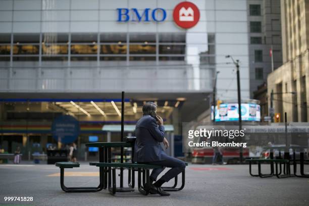 Man holds a smartphone while sitting outside of a Bank of Montreal building in the financial district of Toronto, Ontario, Canada, on Wednesday, July...